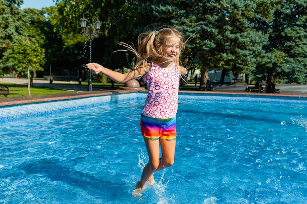 Милая веселая маленькая девочка играет в фонтане. Ребенок веселится в летнем парке у городского фонтана.