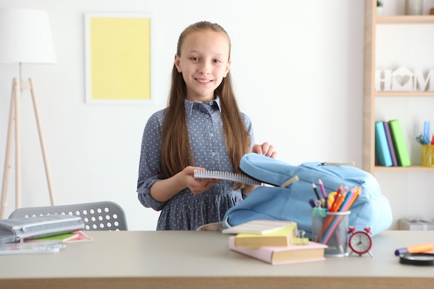 Cute cheerful schoolgirl puts stationery in a backpack