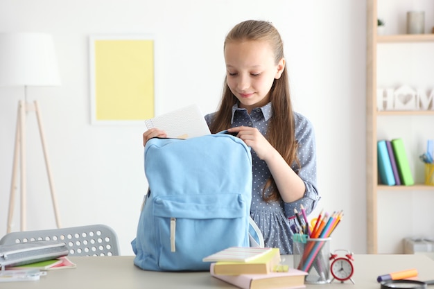 Cute cheerful schoolgirl puts stationery in a backpack