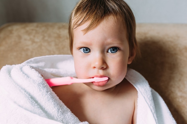 彼女は歯ブラシで彼の歯を磨く大きな白いタオルでかわいい子供