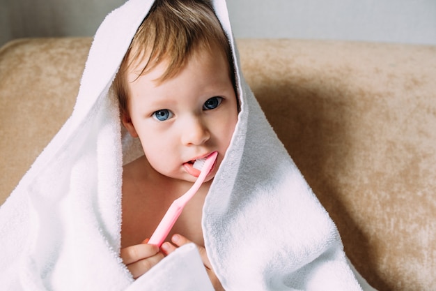 Bambino carino con un grande asciugamano bianco si lava i denti con lo spazzolino da denti