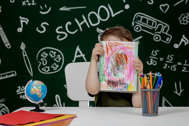 写真 宿題をしている可愛い子供 机で絵を描く賢い子供 学校の少年 小学校の生徒が職場で描く 子供は学習を楽しんでいます 家庭教育 学校に戻る 小さな男の子は学校のレッスン