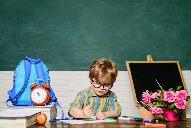 Милый ребенок мальчик делает домашнее задание умный ребенок рисует за партой школьник ученик начальной школы рисует