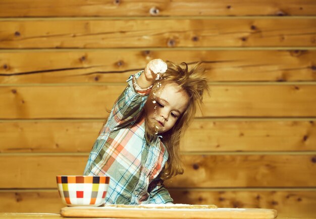 Bambino sveglio che cucina con pasta, farina e ciotola su legno