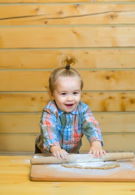 Cute child cooking with dough flour and wood rolling pin