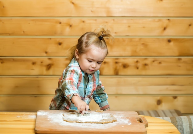 Cute child cooking with dough, flour on wood