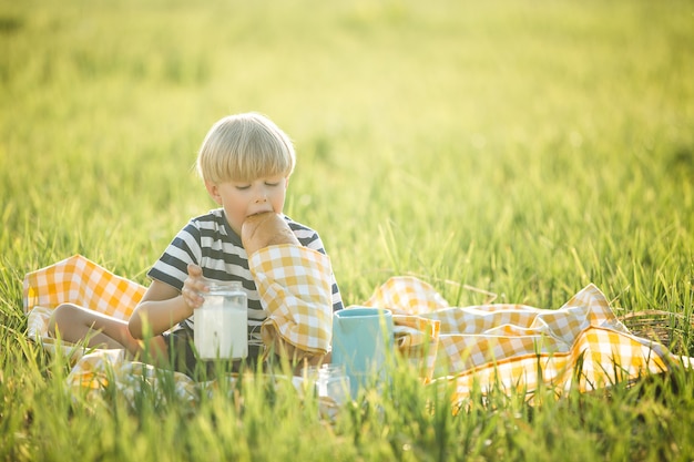 かわいい子が屋外で牛乳を飲みます。ピクニックに快活な少年