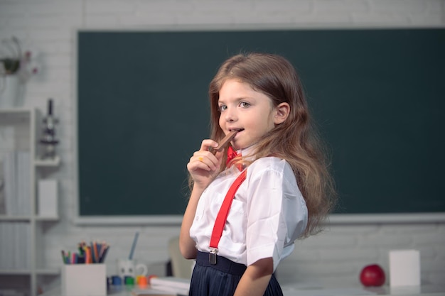 学校でチョコレート菓子を食べるかわいい子。子供は黒板の背景でクラスで学んでいます。