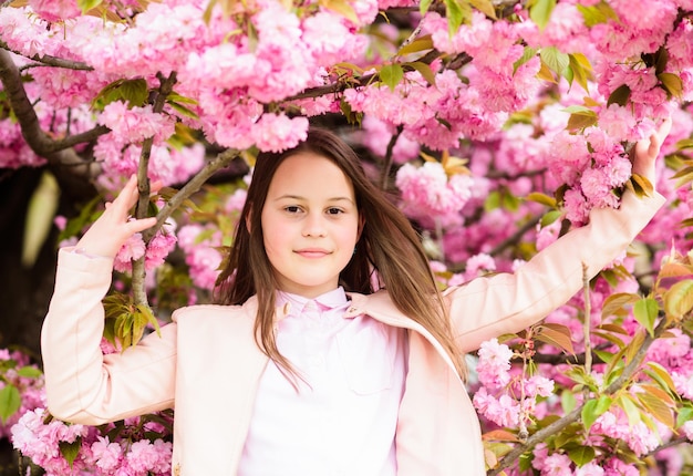 Cute child enjoy warm spring day Aromatic blossom concept Girl tourist posing near sakura Tender bloom Child on pink flowers of sakura tree background Girl enjoying cherry blossom or sakura