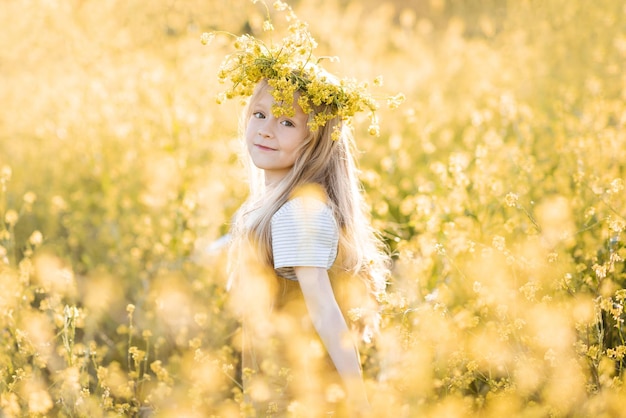 Photo cute child girl 4-5 year old wear floral wreath stand in yellow flower meadow outdoor over nature