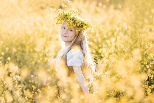 Cute child girl 4-5 year old wear floral wreath stand in yellow flower meadow outdoor over nature