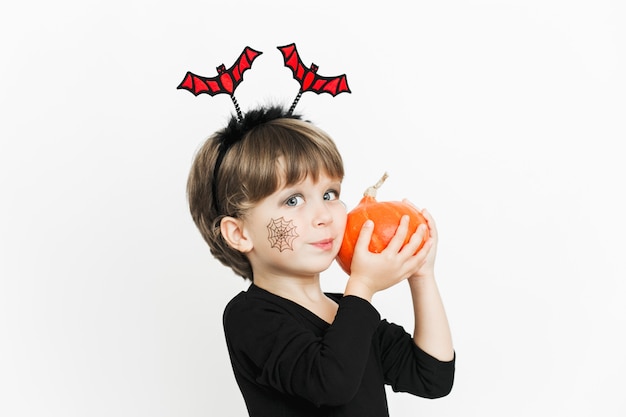 Cute child girl in black costume and makeup with pumpkin having fun on Halloween celebration