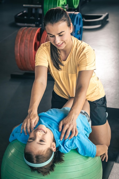 Cute child girl stretching on pilates fitness ball with mom in gym