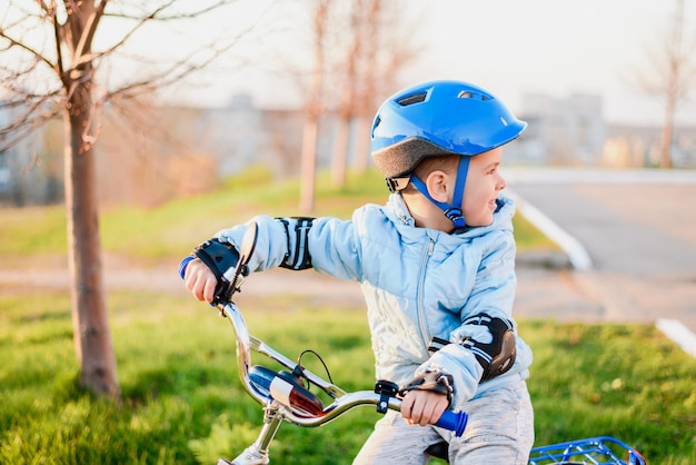 Cute child in helmet learns and rides a bike on a sunny day at sunset