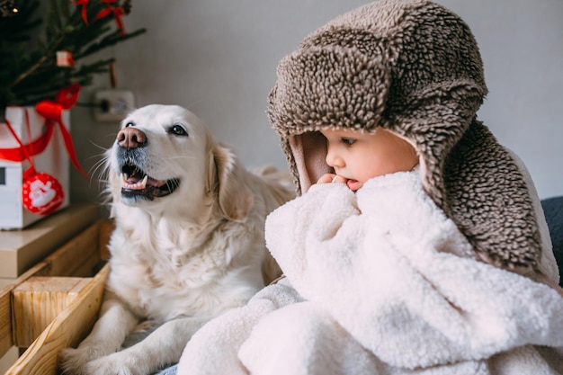 Foto bambino carino e il suo labrador retriever a casa sul letto vicino all'albero di natale