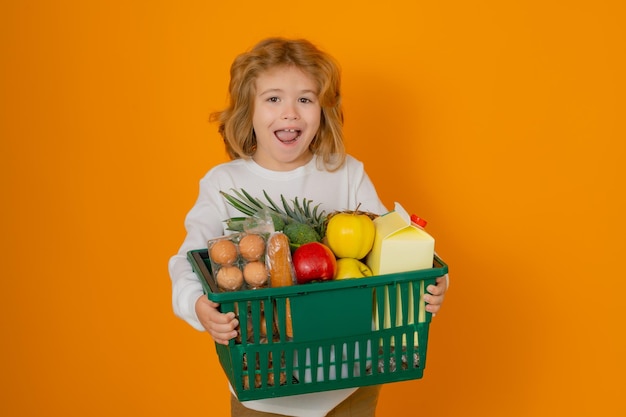 Cute child hold shopping cart full of groceries kid holds shopping basket over yellow background sto