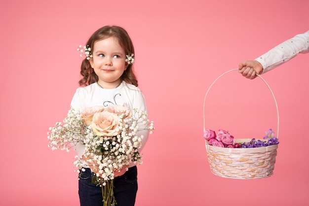 Foto bambino sveglio che tiene il mazzo di fiori primaverili e guardando la mano che tiene il cesto con i fiori sul lato sinistro