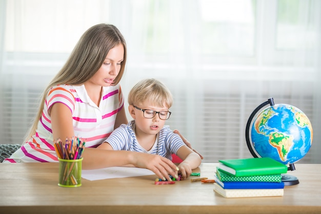 Bambino sveglio che impara una lezione con sua madre. famiglia facendo i compiti insieme. mothe spiega al suo piccolo scolaretto come svolgere un compito.