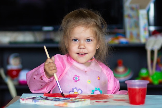 Милый ребенок рисует кистью и красочными красками на бумаге
