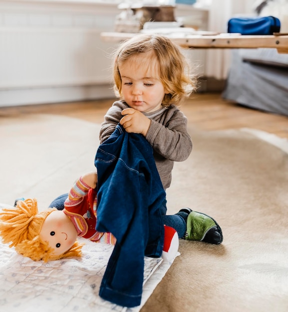 Photo cute child playing with doll on rug at home