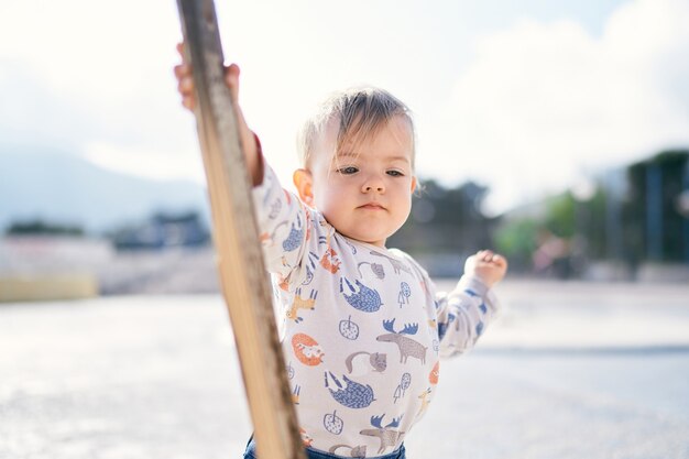 Cute child stands on the beach and holds a stick in his hand