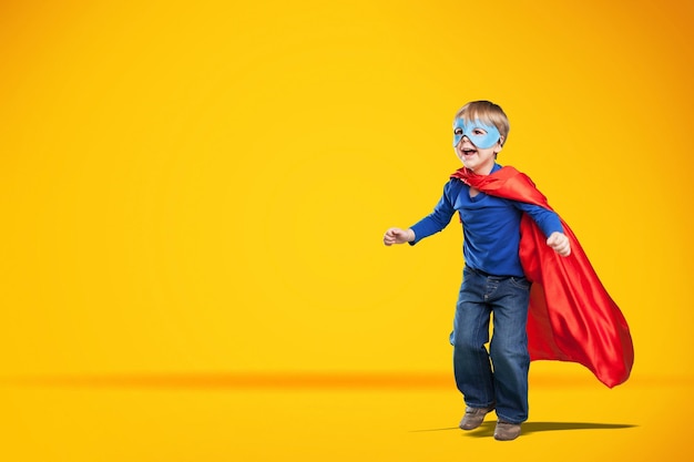 Cute child in superhero cape smiling and raising fist up