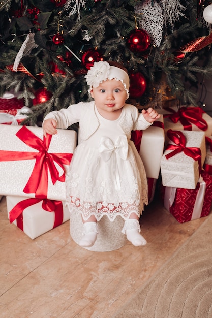 Cute child in white dress posing under christmas tree.