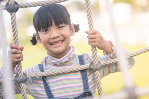 귀여운 아이들. 모험 공원에서 밧줄 놀이터 구조에 등반 하는 아시아 소녀