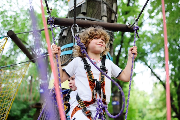 Cute children - a boy in adventure park is engaged in rock climbing or pass obstacles on the rope road.