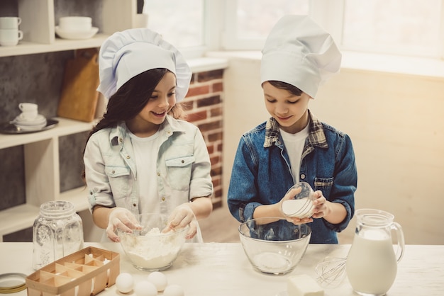 Cute children in chef hats are preparing dough.