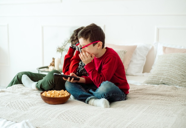 自宅で3Dメガネでテレビを見ながらポップコーンを食べるかわいい子供たち。