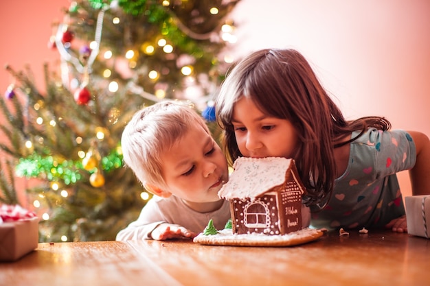 Cute children nibbling a gingerbread cookie house at christmas time