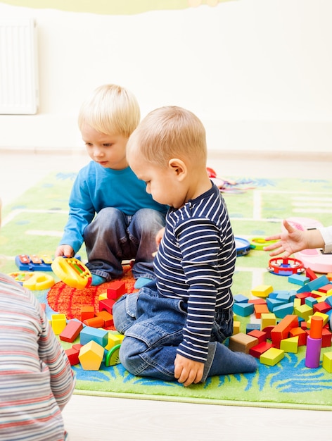 かわいい子供たちが幼稚園で遊んでいます。小さな男の子は彼の友人のおもちゃに興味を持っています