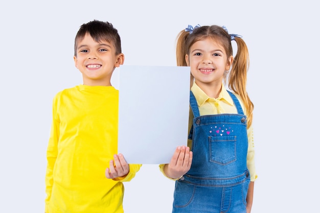 Bambini carini con un sorriso felice stanno posando con un foglio di carta bianco per la tua pubblicità.