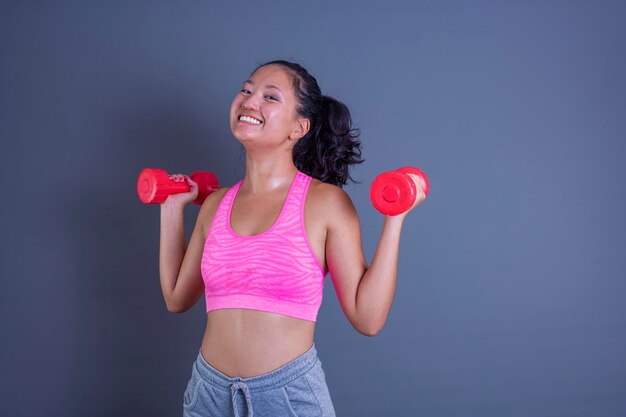 Cute chinese sporty girl smiling while looking straight ahead and holding a dumbbell in her hands