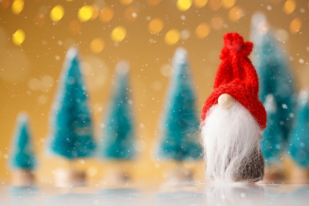 Cute christmas gnome is sitting and waiting for his presents for christmas on yellow bokeh background.