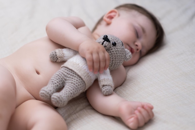 Cute chubby baby sleeping on back holding knitted bear toy with hand