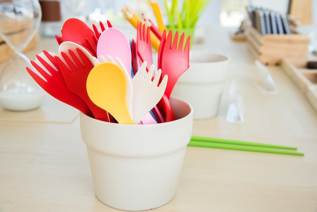 cute colorful plastic spoon and fork in cup on wooden table