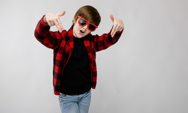 Cute confident little caucasian boy in checkered shirt in red sunglasses fooling on grey 