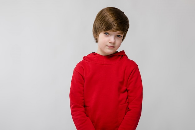 Cute confident little caucasian boy in red sweater on grey background