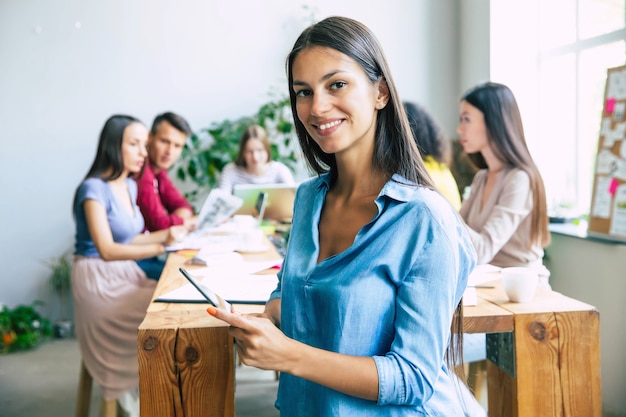 Cute confident modern business woman in casual clothes looks at the camera and smiling. Modern start-up business team in office