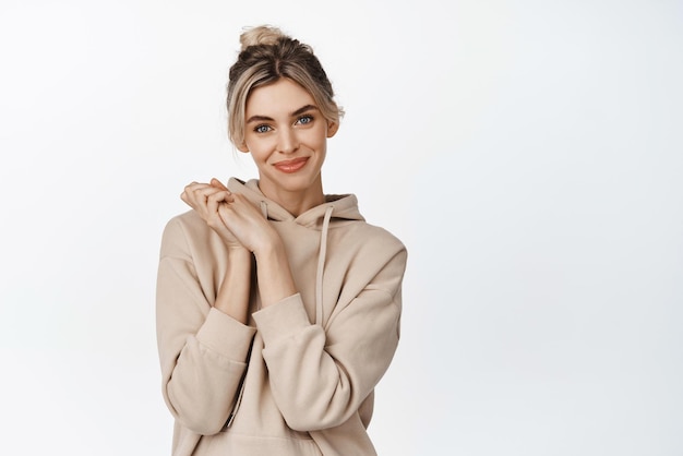 Cute coquettish girl hope to achieve something clasp hands together and looking hopeful smiling at camera standing over white background