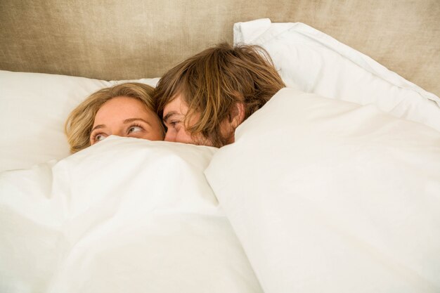 Cute couple cuddling under the blanket in their bed