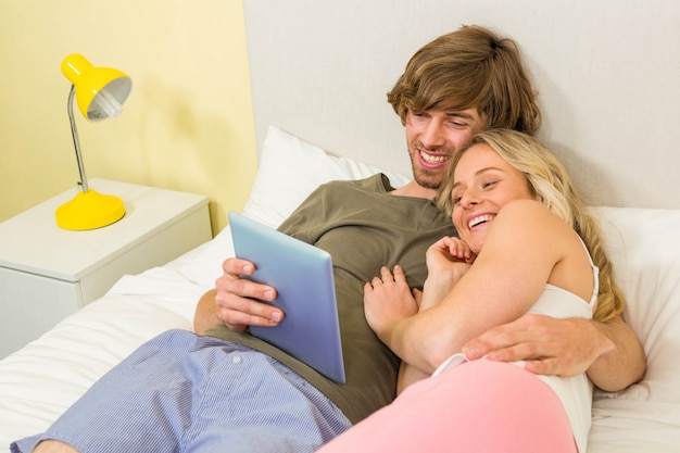 Cute couple cuddling and using tablet in the bedroom