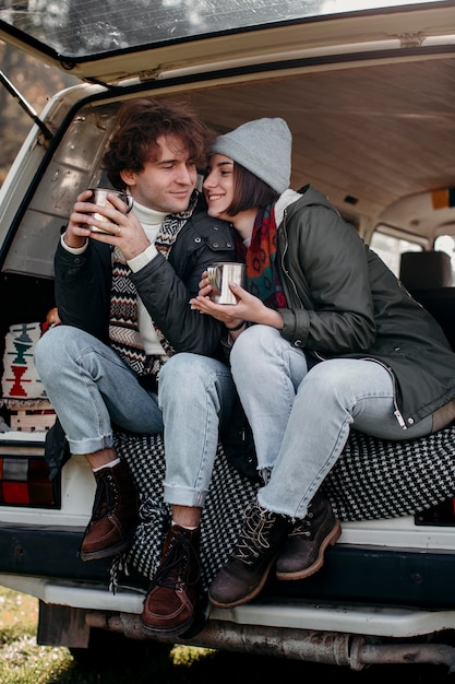 Photo cute couple holding cups of coffee in a van