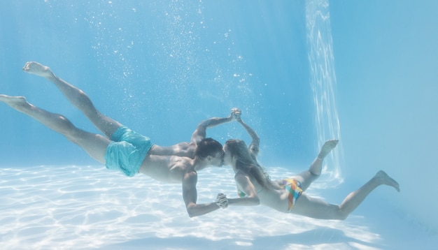 Cute couple holding hands underwater in the swimming pool