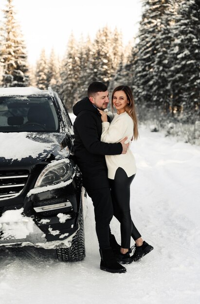 Cute couple hugging near car in winter man and woman in love look at each other near the car