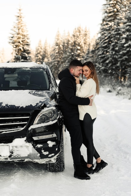 Cute couple hugging near car in winter man and woman in love look at each other near the car