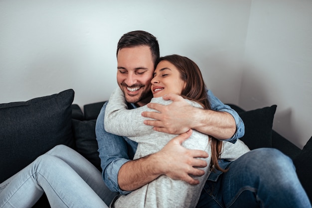 Cute couple hugging on the sofa, with their eyes closed, wearing casual outfits. 