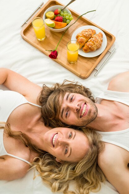 Cute couple lying in bed next to a breakfast tray in their bedroom